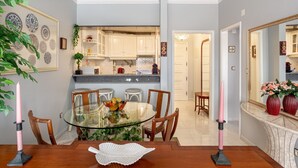 A dining area with a glass table, wooden chairs, and a vase of flowers. - JOIVY Vibrant 2-bed flat w/ balcony (COSTA DE CAPARICA)