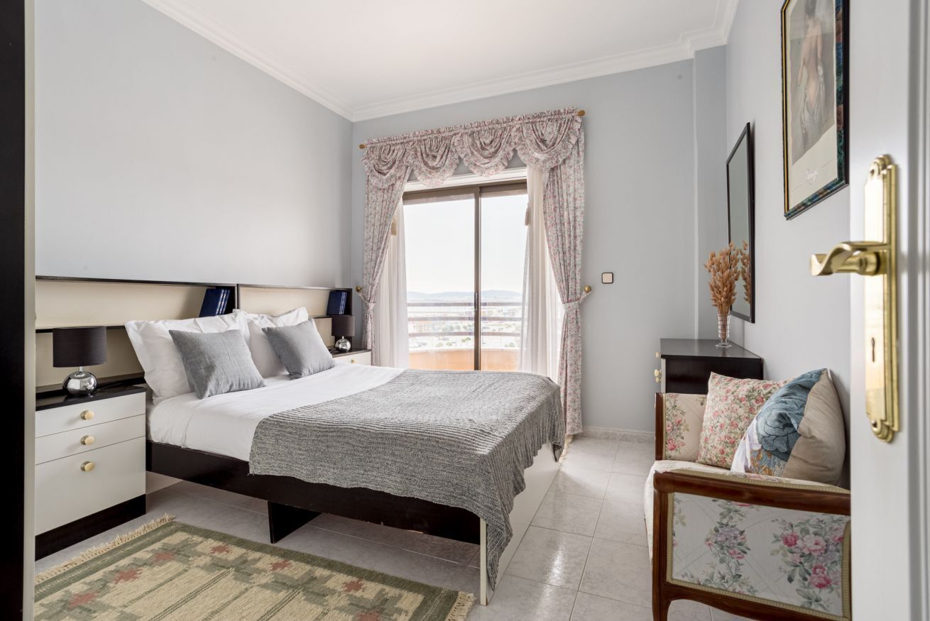 Quarto com cama, mesas de cabeceira, um sofá e vista para o exterior.