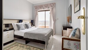 A bedroom with a bed, bedside tables, a nightstand, a window with curtains, a sofa, and a view of the outside. - JOIVY Vibrant 2-bed flat w/ balcony (COSTA DE CAPARICA)