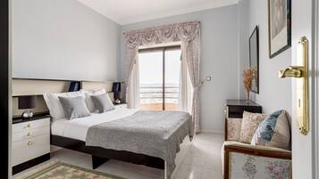 Quarto com cama, mesas de cabeceira, um sofá e vista para o exterior.
