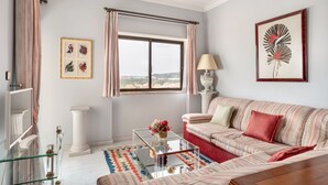 A living room with a striped sofa, a glass coffee table, a white column, a window with curtains, and a framed picture on the wall. - JOIVY Vibrant 2-bed flat w/ balcony (COSTA DE CAPARICA)