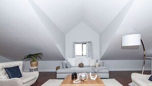Un loft moderno con techo alto, sofá gris, mesa de centro de madera y lámpara de pie.