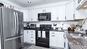 Cocina moderna con armarios blancos, electrodomésticos de acero inoxidable y encimeras de granito.