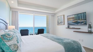 A hotel room with a large bed, a balcony with a view of the sea, a television, and a painting.