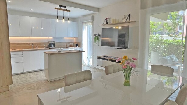 A modern kitchen with white cabinets, a central island, and a dining area with a glass table and chairs. - Apartment for 6 people - Air conditioning - Wifi - Downtown - Sainte Maxime (STE MAXIME)