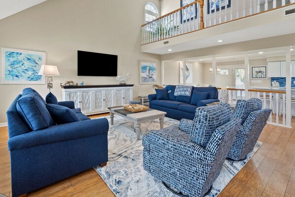 A spacious living room with a large TV, blue sofas, patterned chairs, and a white cabinet.