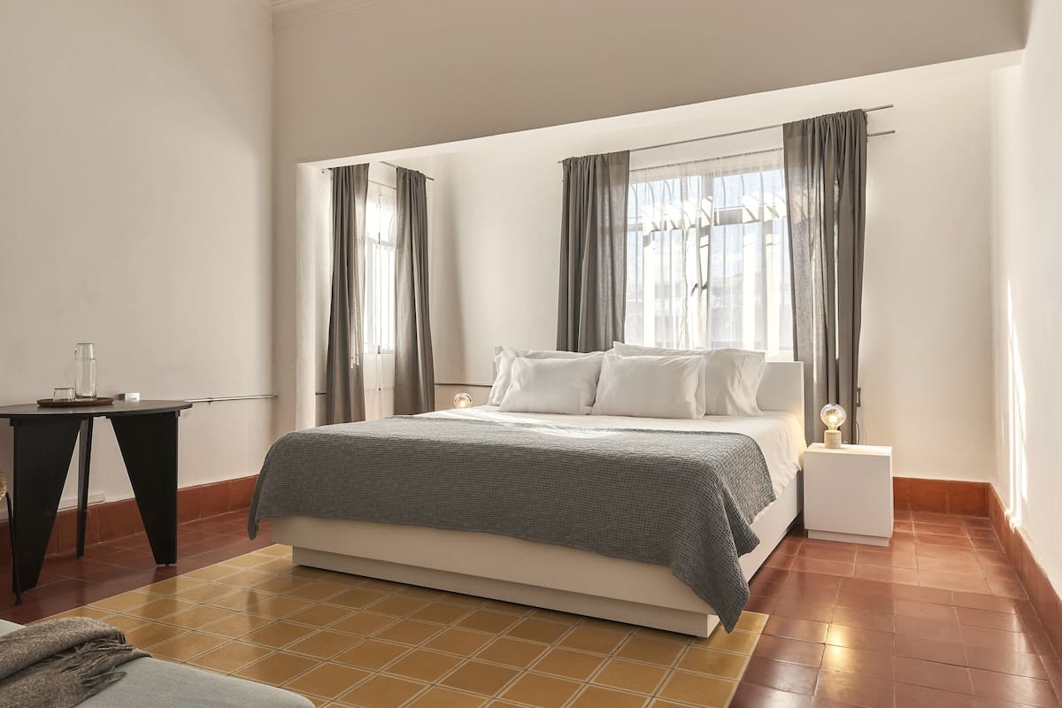 Une chambre à coucher moderne avec un grand lit, une table de chevet et une petite table avec un verre.