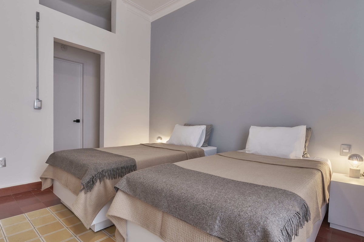 Une chambre d’hôtel avec deux lits, chacun doté d’une table de chevet et d’une lampe, d’une porte et d’un luminaire fixé au plafond.