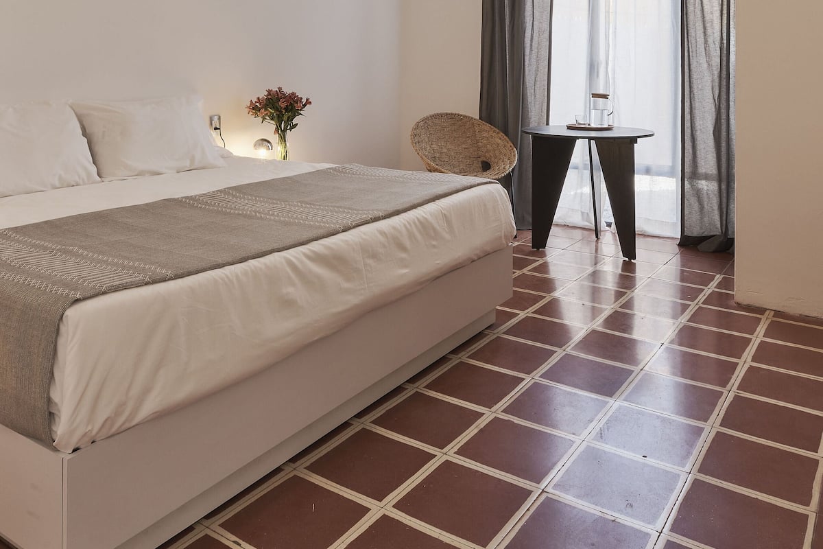 Une chambre à coucher avec un lit, un ventilateur de plafond, une fenêtre avec des rideaux, une petite table avec une tasse et un vase avec des fleurs.