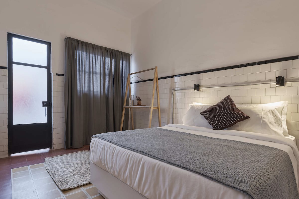 Une chambre à coucher avec un lit, une échelle en bois, une fenêtre avec des rideaux et un mur recouvert de carreaux.