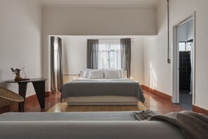 Une chambre d’hôtel moderne avec un grand lit, une petite table ornée d’un vase et une vue sur la ville par la fenêtre.
