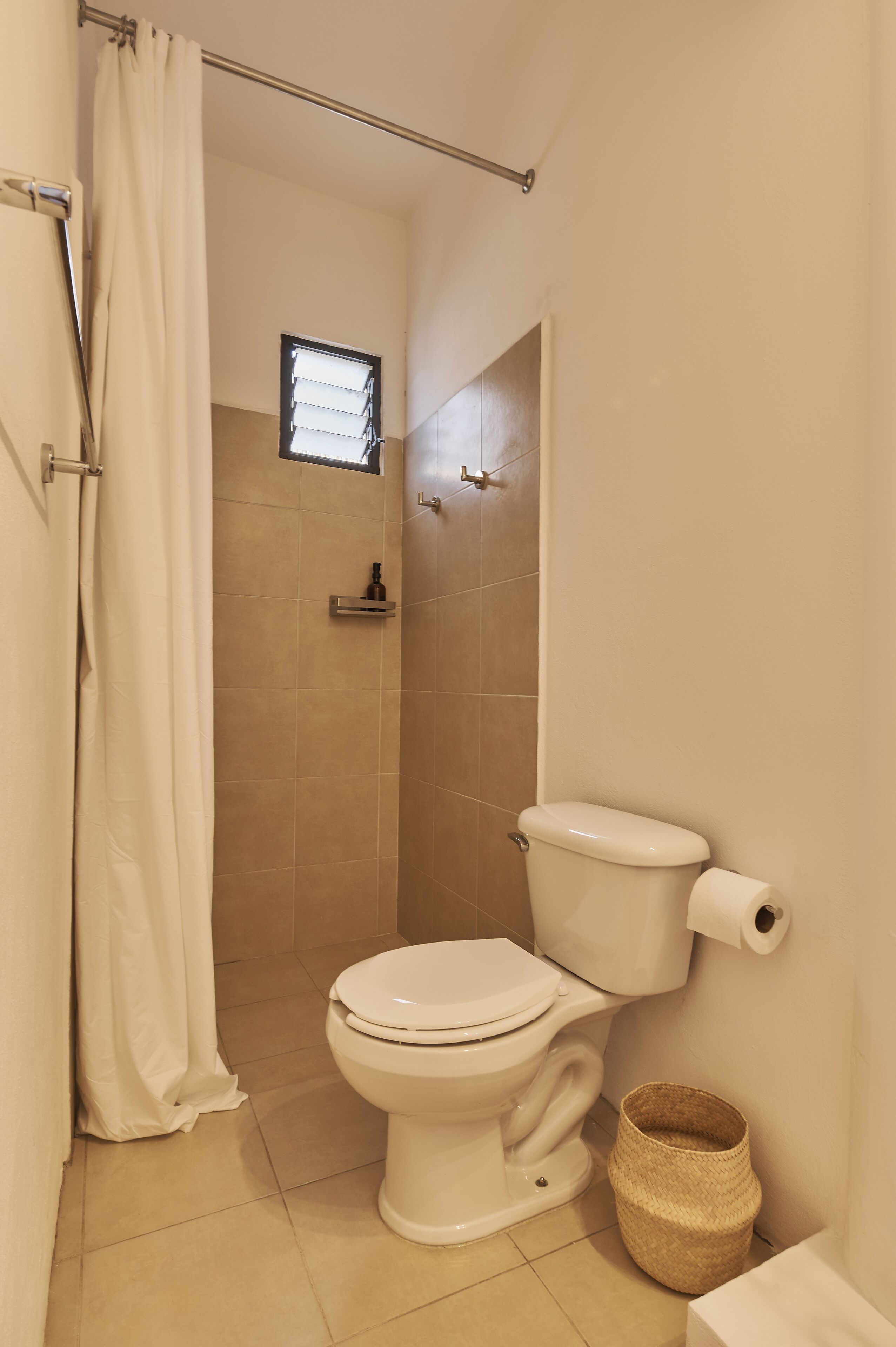 A bathroom with a toilet, a shower, and a small window.