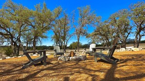Zona d'estar exterior amb cadires Adirondack i taules de picnic, envoltada d'arbres i un cel blau clar.