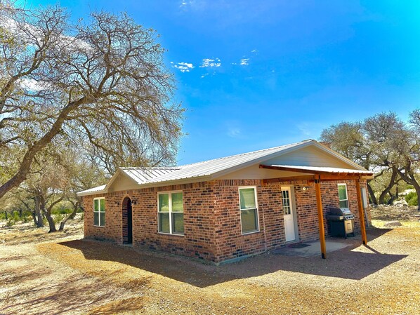 A small brick building with a metal roof, a covered porch, and a barbecue area.