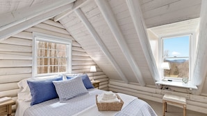 A cozy attic bedroom with a large bed, a small table, and a window with a view.