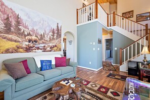 A living room with a large wall mural, a light blue sofa with colorful cushions, a wooden coffee table, and a staircase leading to an upper level.