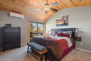 A bedroom with a bed, a dresser, a bench, a ceiling fan, and a view of the outdoors.