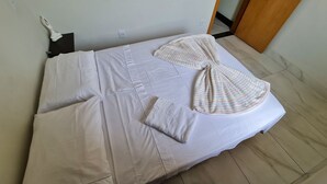 Una cama bien tendida con ropa de cama blanca y una manta a rayas, un almohadón blanco y una toalla doblada.