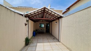 Un porche estrecho y cubierto con piso de baldosas, una pérgola de madera y vista hacia una casa.