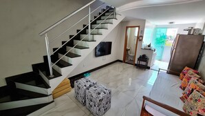Una sala de estar moderna con escalera, televisor de pantalla plana, zona de cocina y vistas al exterior.