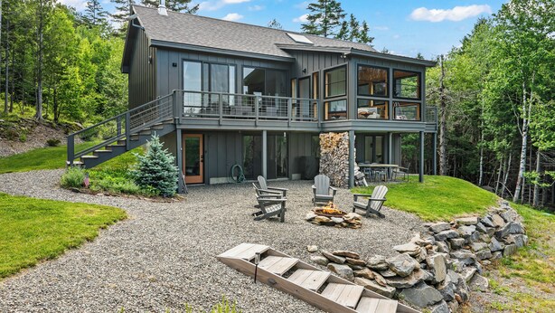 Een tweelaags huis met een balkon, buiten zitplaatsen en een vuurkorf van natuursteen.