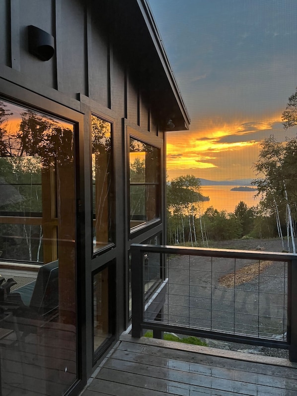 A modern building with large windows and a balcony overlooking a sunset over a body of water.