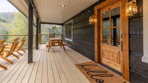Une terrasse en bois avec un banc et des chaises, une porte en bois avec des panneaux de verre, et une vue sur les arbres.