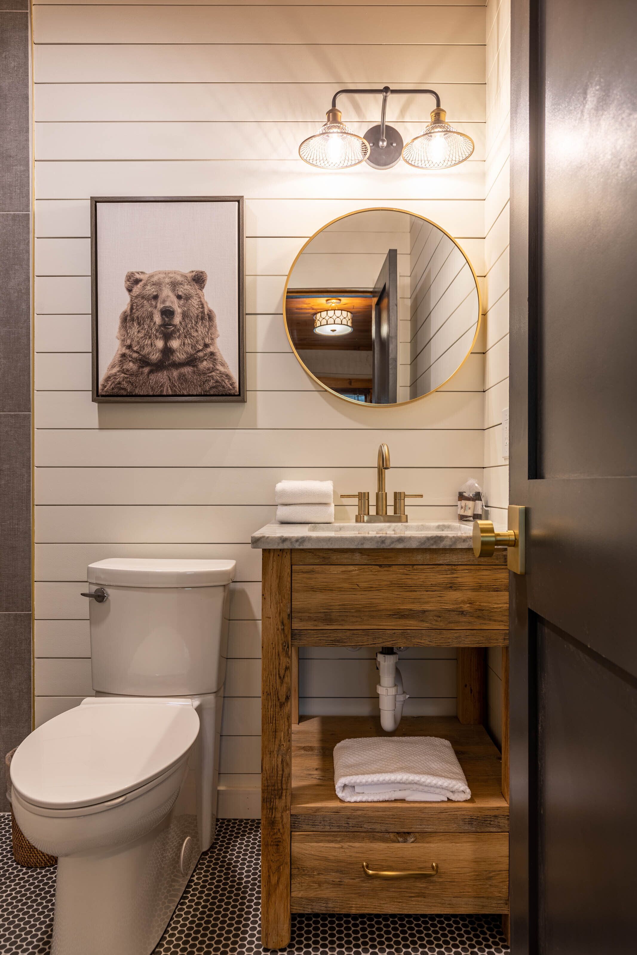 A bathroom with a toilet, sink, wooden vanity, and a mirror.
