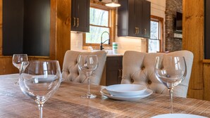 Une table à manger avec quatre verres à vin, une assiette blanche et un bol. La table est placée dans une pièce dotée de meubles en bois foncé et d’un mur en pierre.