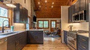 Une cuisine moderne avec des meubles de couleur sombre, un mur en pierre et un plafond en bois.