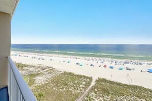 Une vue sur la plage depuis un balcon, avec une plage de sable, des parasols et un ciel dégagé.
