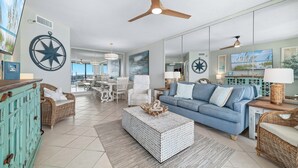 A spacious living room with a blue sofa, a white coffee table, and a ceiling fan. - Bluewater 1005 |  Beachfront Condo | Private Balcony | Resort Amenities | My Beach Getaways (Orange Beach)