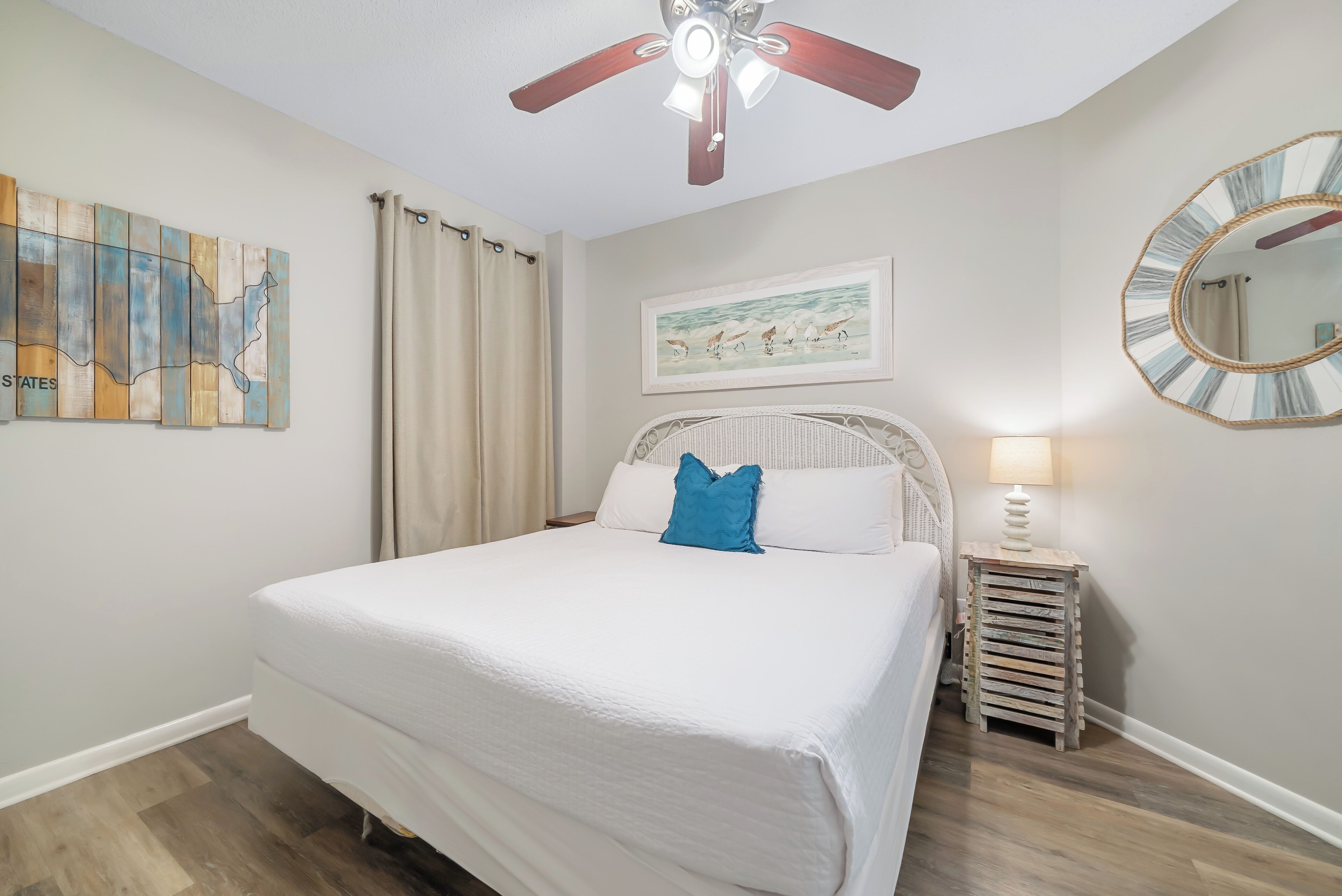 Un dormitorio con cama, ventilador de techo, mapa en la pared, un cuadro enmarco, espejo y mesita de noche.