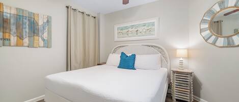 Un dormitorio con cama, ventilador de techo, mapa en la pared, un cuadro enmarco, espejo y mesita de noche.