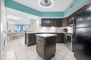 A modern kitchen with dark cabinets, a black refrigerator, and a tiled floor. - Bluewater 1005 |  Beachfront Condo | Private Balcony | Resort Amenities | My Beach Getaways (Orange Beach)