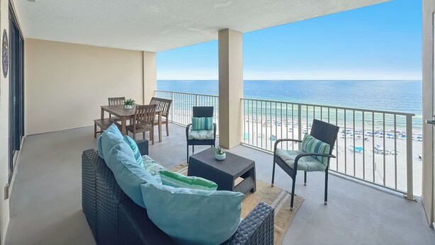 A balcony with a view of the beach, a sofa, chairs, a table, and a small plant. - Bluewater 1005 |  Beachfront Condo | Private Balcony | Resort Amenities | My Beach Getaways (Orange Beach)