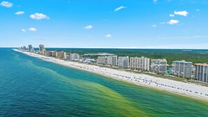 A coastal hotel with multiple high-rise buildings, a beachfront, and a clear blue sky. - Bluewater 1005 |  Beachfront Condo | Private Balcony | Resort Amenities | My Beach Getaways (Orange Beach)