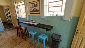 Una cocina con salpicadero de azulejos azules, taburetes de madera, encimera negra y un cubo de basura.