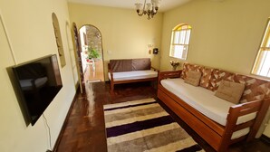Una sala de estar con un sofá de madera, un televisor, un tapete estampado y una ventana con barrotes.