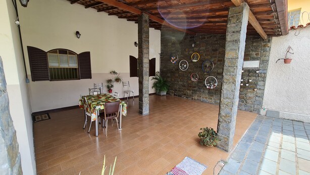 Un patio techado con una mesa y sillas de comedor, pilares de piedra y piso de baldosas.