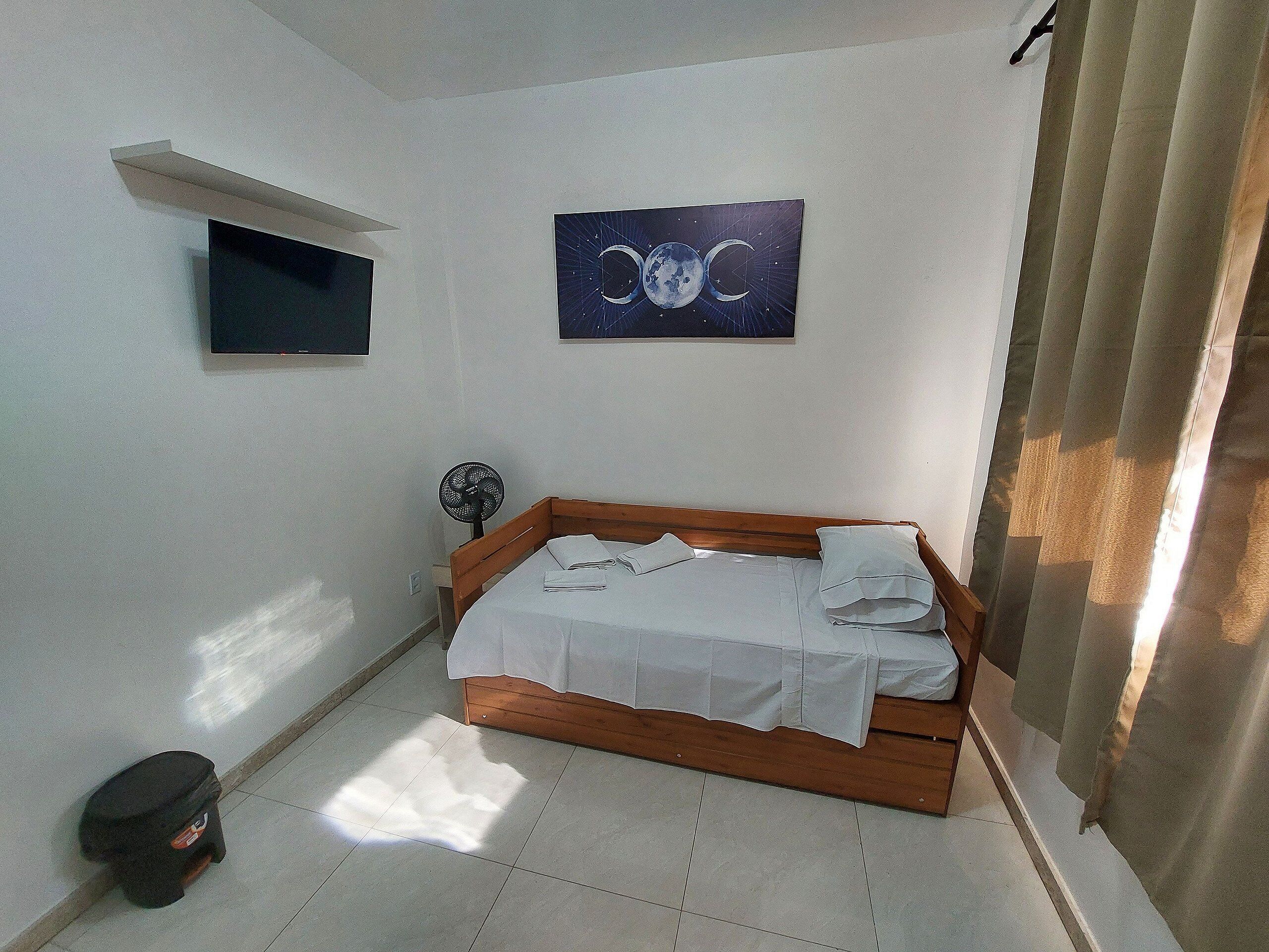 Een slaapkamer met een bed, een aan de muur bevestigde televisie en een plafondventilator.