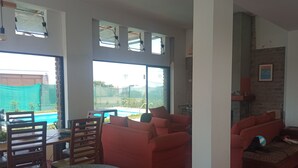 Un vaste espace de vie avec vue sur la piscine, des canapés rouges et une table à manger avec des chaises.