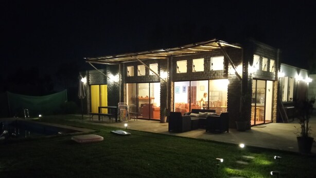 Une maison moderne dotée d’une façade en verre, d’un espace extérieur aménagé et d’une piscine.