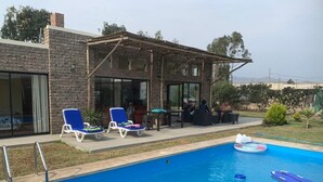Une piscine avec des chaises longues, une pergola en bois et un bâtiment en briques doté de grandes fenêtres.