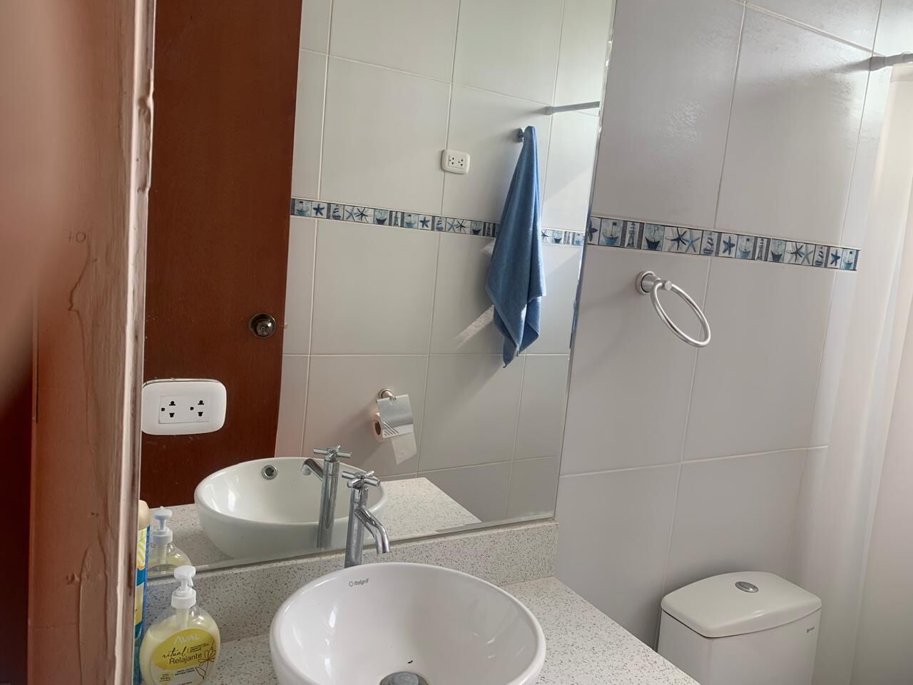 Un baño con un lavamanos blanco, un espejo, un perchero para toallas y un inodoro.