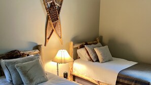 A cozy room with two wooden beds, a wall-mounted decorative item, and a lamp. - Newly Remodeled Condo on Golf Course, A/C, Pet Friendly, SHARC passes, Bikes. (Sunriver)