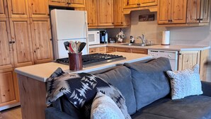 A modern kitchen with wooden cabinets, a built-in oven, and a central island with a gray sofa. - Newly Remodeled Condo on Golf Course, A/C, Pet Friendly, SHARC passes, Bikes. (Sunriver)