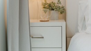 A white bedside table with a lamp, a glass pitcher, and a small plant. - Missouri St · 5 Mins to Beach! New 3bd Getaway / Central AC! (San Diego)
