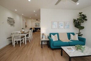 A modern living room with a teal sofa, white dining chairs, and a coffee table.