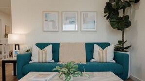 A teal sofa with striped pillows, a marble coffee table with a plant, and framed abstract art on the wall. - Missouri St · 5 Mins to Beach! New 3bd Getaway / Central AC! (San Diego)